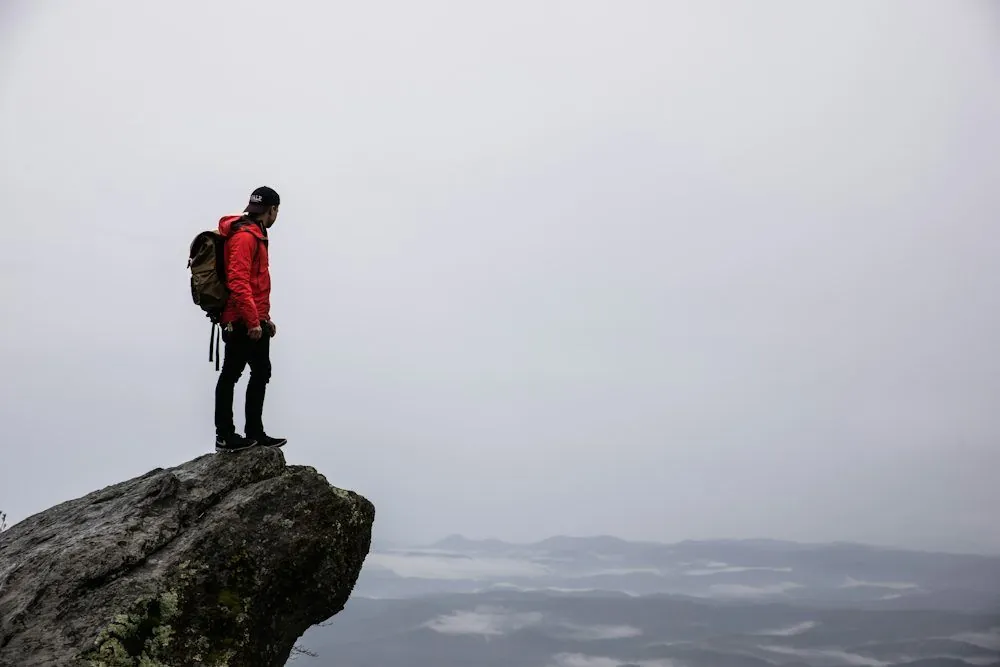 Man in a red jacket standing at the peak of a mountain